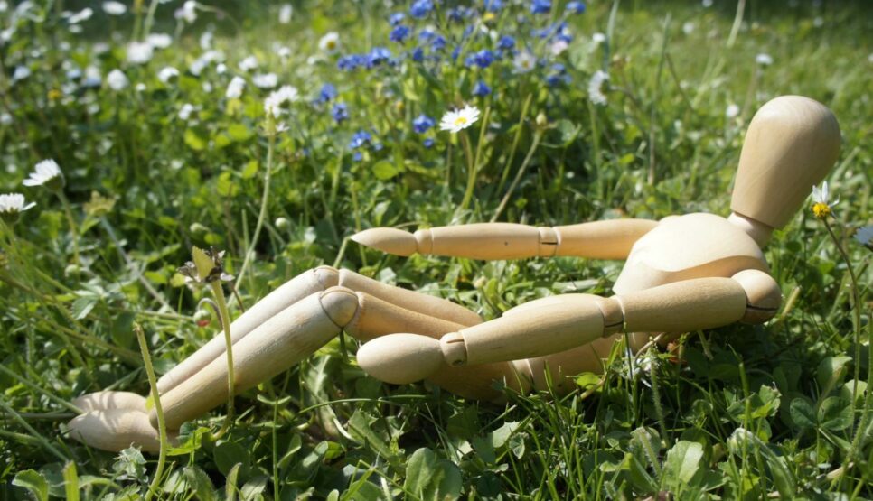 Holzpuppe beim "Halfrollback" (Pilates) auf einer Blumenwiese
